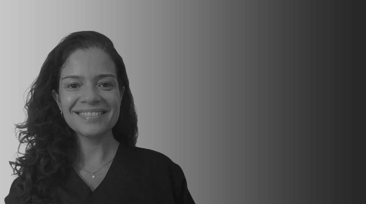 Mulher branca de cabelo preto longo e ondulado sorri para foto. Ela veste blusa escura. É Claudia Inglez.