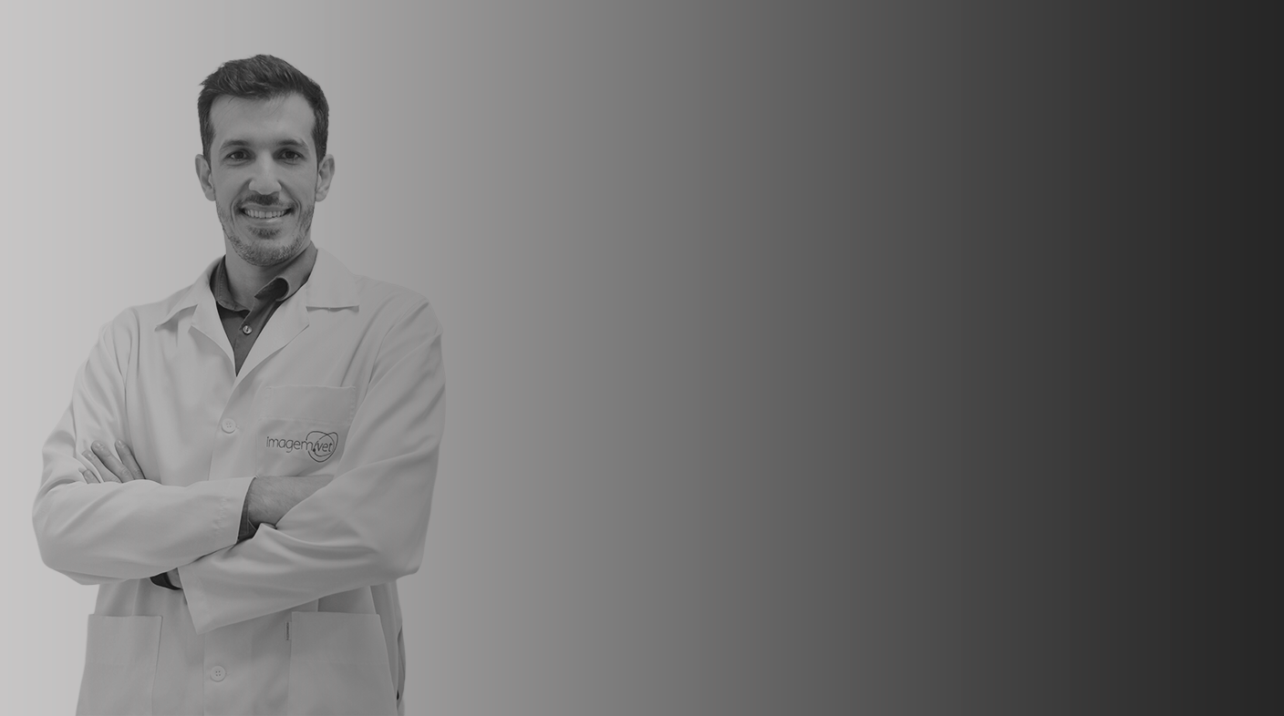 Homem branco jovem vestindo jaleco branco de médic-veterinário e blusa escura em pé, sorrindo para foto. Ele está com os braços cruzados sobre o peito. É Paulo Frazão.