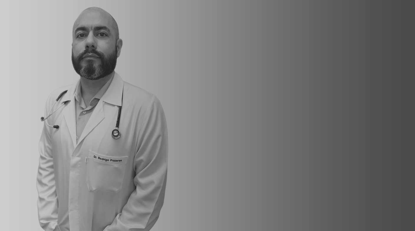 Homem branco careca e de barba preta usa jaleco branco de médico-veterinário e estetoscópio. É Rodrigo Prazeres.