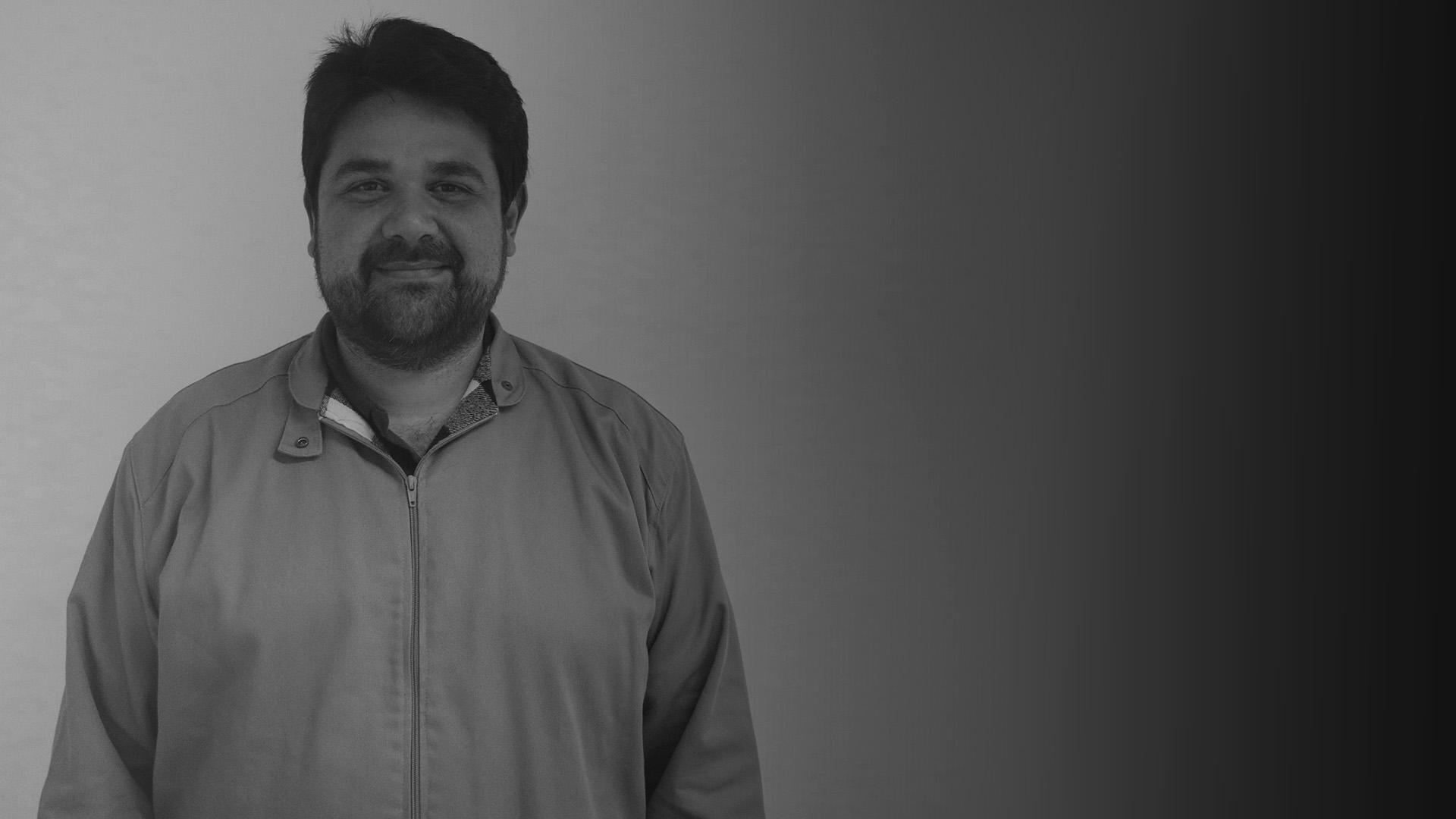 Homem branco de cabelos e barba preta sorrindo para foto. Ele usa casaco com zipper. É Fabrício Rassy.