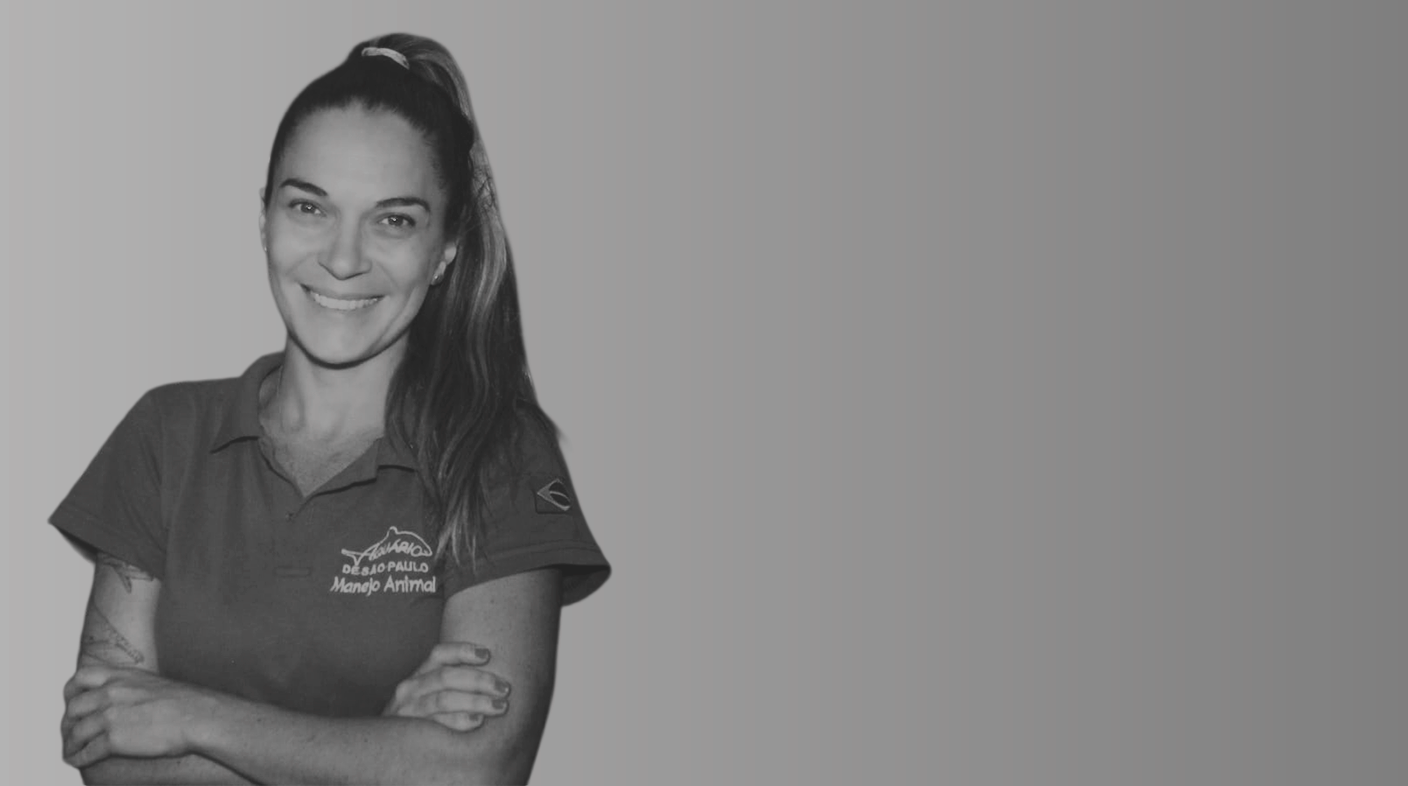 Mulher branca de olhos claros e cabelo liso longo e castanho claro em pé, sorrindo para foto. Ela usa blusa com os dizeres: Aquário de São Paulo. É a dra. Laura Reisfeld.