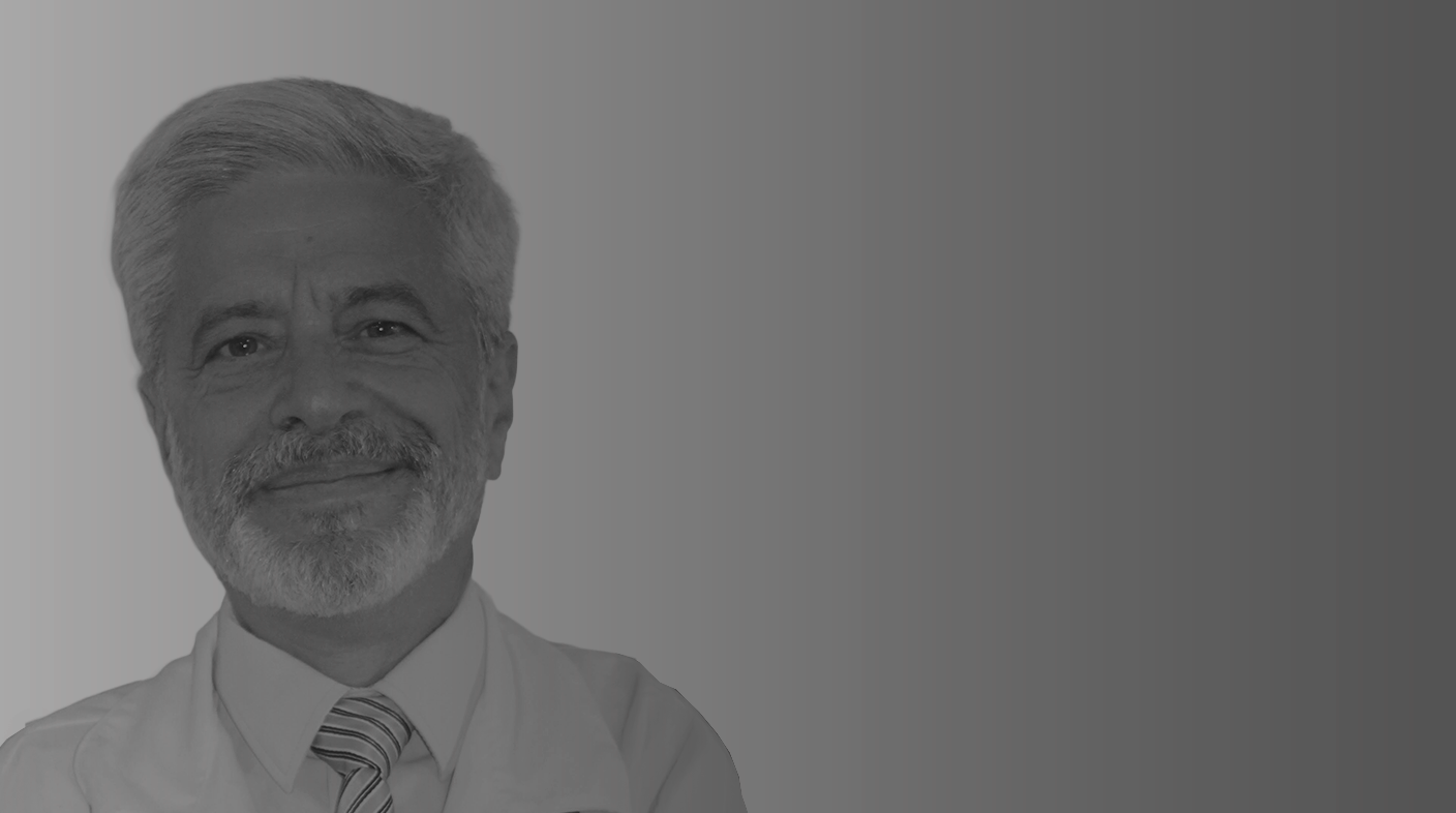 Homem branco com cabelos brancos curtos e barba usando jaleco branco, camisa social branca e gravata. É o dr. Luiz Roberto Biondi.