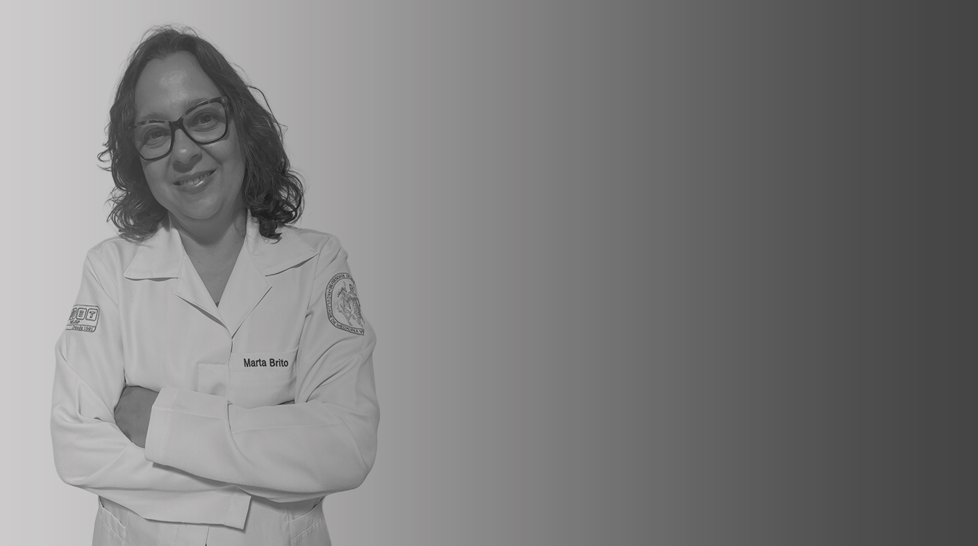 Mulher de fios médios e ondulados, veste jaleco de médico-veterinária e óculos de armação quadrada, sorrindo para foto. É a dra. Marta Brito.