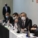 Presidente do CRMV-SP, Mário Eduardo Pulga, está falando ao microfone de mesa, sentado, de máscara, vestindo terno e uma gravata listrada nas cores azul marinho e vermelho. Ao seu lado estão presidentes de outros regionais e em pé, ao fundo da sala, dois profissionais da equipe do setor de eventos do Federal.