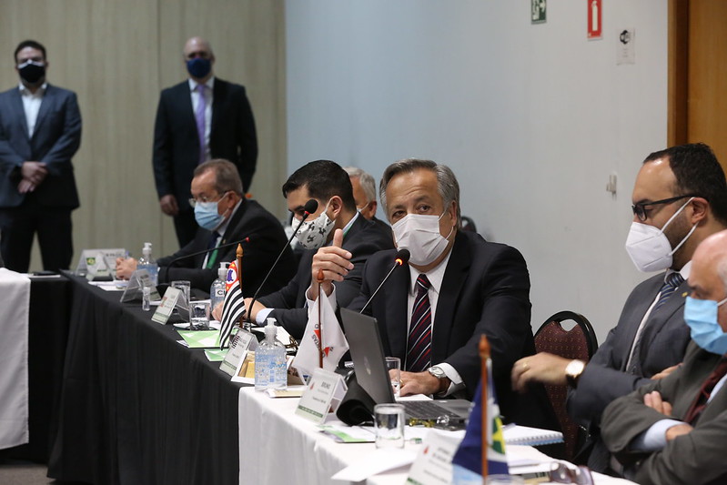 Presidente do CRMV-SP, Mário Eduardo Pulga, está falando ao microfone de mesa, sentado, de máscara, vestindo terno e uma gravata listrada nas cores azul marinho e vermelho. Ao seu lado estão presidentes de outros regionais e em pé, ao fundo da sala, dois profissionais da equipe do setor de eventos do Federal.