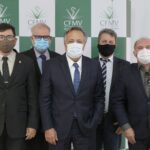 Membros da nova Câmara Técnica de Medicina Veterinária do CFMV possam, todos de terno e máscara, em frente ao painel quadriculado nas cores verde e branco e logo do Conselho Federal.