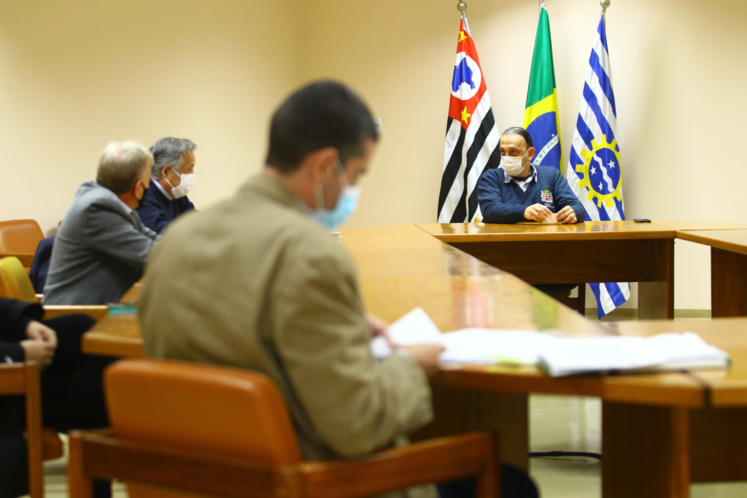 Sentados a mesa conversando estão o presidente, o vice-presidente e o coordenador técnico médico-veterinário do CRMV-SP, e, ao fundo em frente as bandeiras do município, do estado e do Brasil, o prefeito de São José dos Campos.