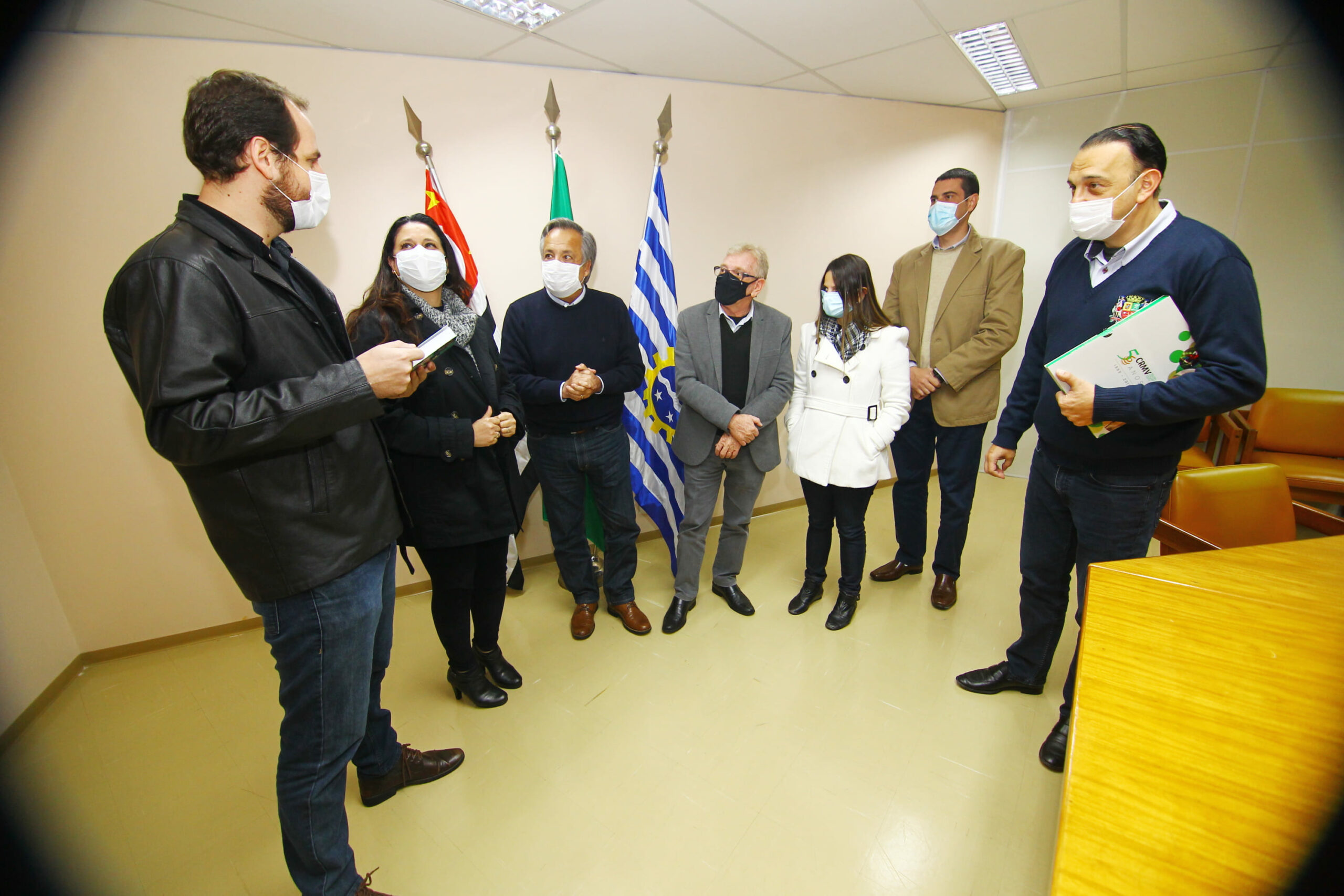 Em pé, conversando frente as bandeiras da cidade, do estado e do Brasil, estão os representantes do CRMV-SP e da Prefeitura de São José dos Campos