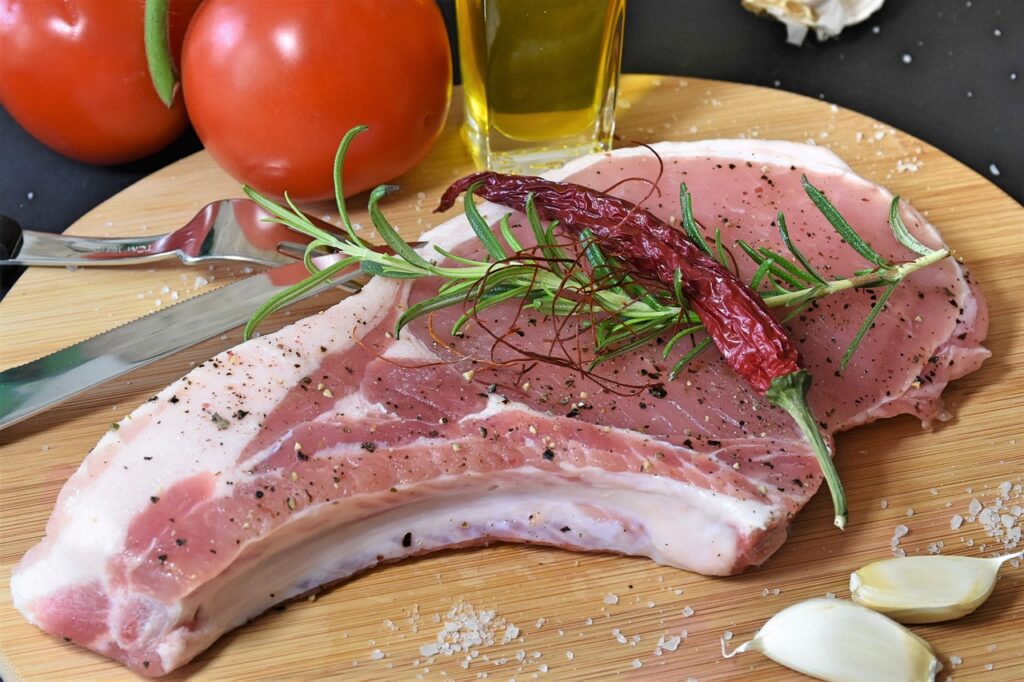 Imagem de um pedaço de carne de porco, com tomates e azeite ao fundo.