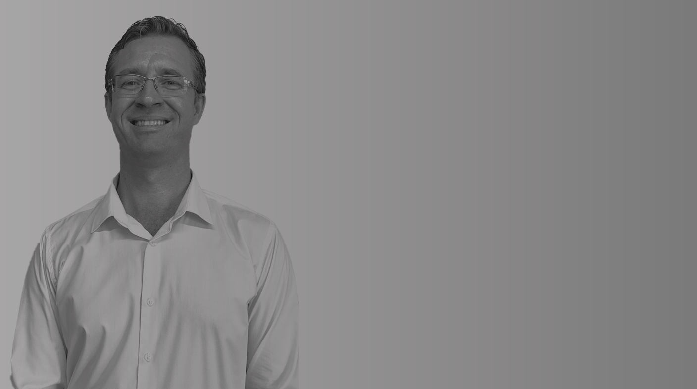 Homem branco em pé sorridente pousando para foto. Ele usa blusa branca social de botões.