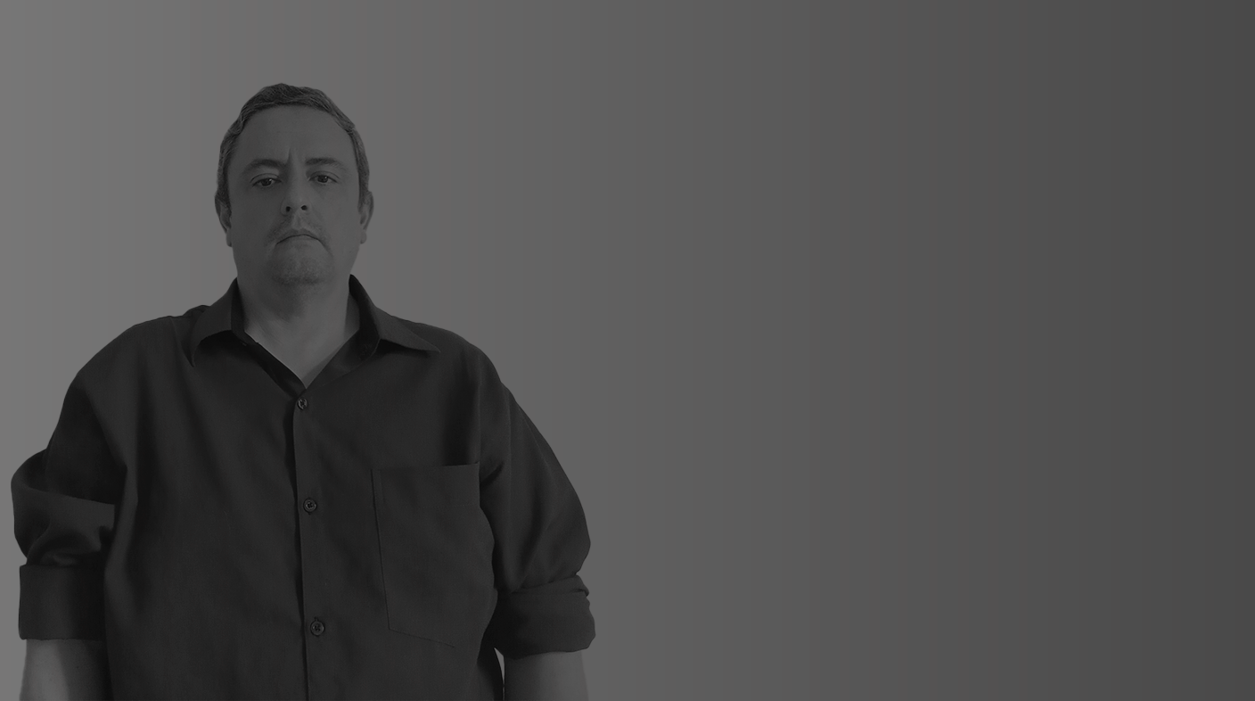 Homem branco em pé pousando sério para foto usando blusa social de mangas longas e botões. É João Gabriel Zerba.