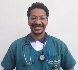 Foto de Augusto Renan Rocha Severo, médico-veterinário e fundador do Afrovet está sorrindo. A imagem mostra o rpofissional de óculos de grau,  com traje médico e estetoscópio no pescoço. 