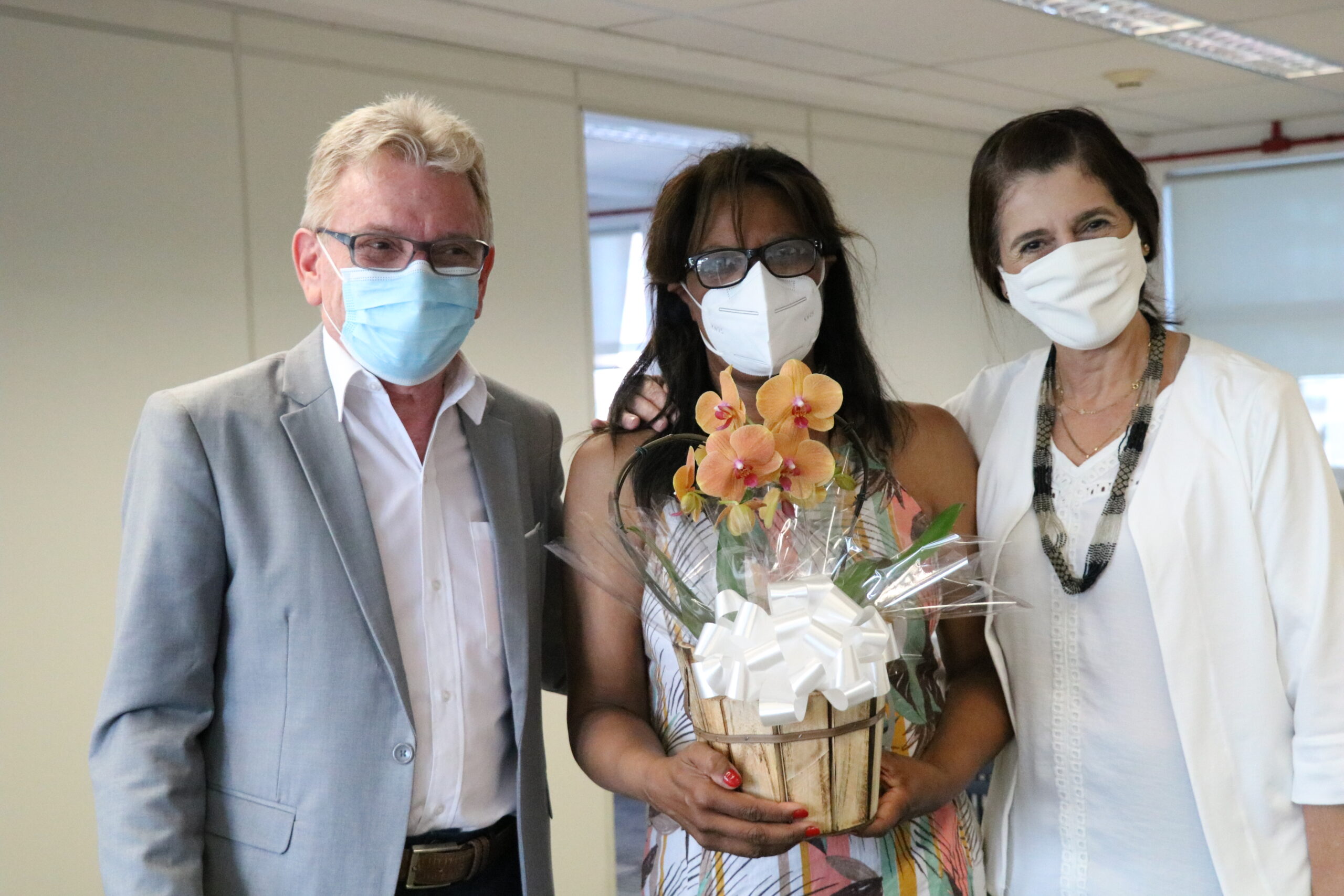 Em pé e usando máscaras a imagem mostra o presidente do Conselho, ao lado da colaboradora Cecília que segura um arrajnjo de flores com a Tesoureira do CRMV-SP à sua direita.