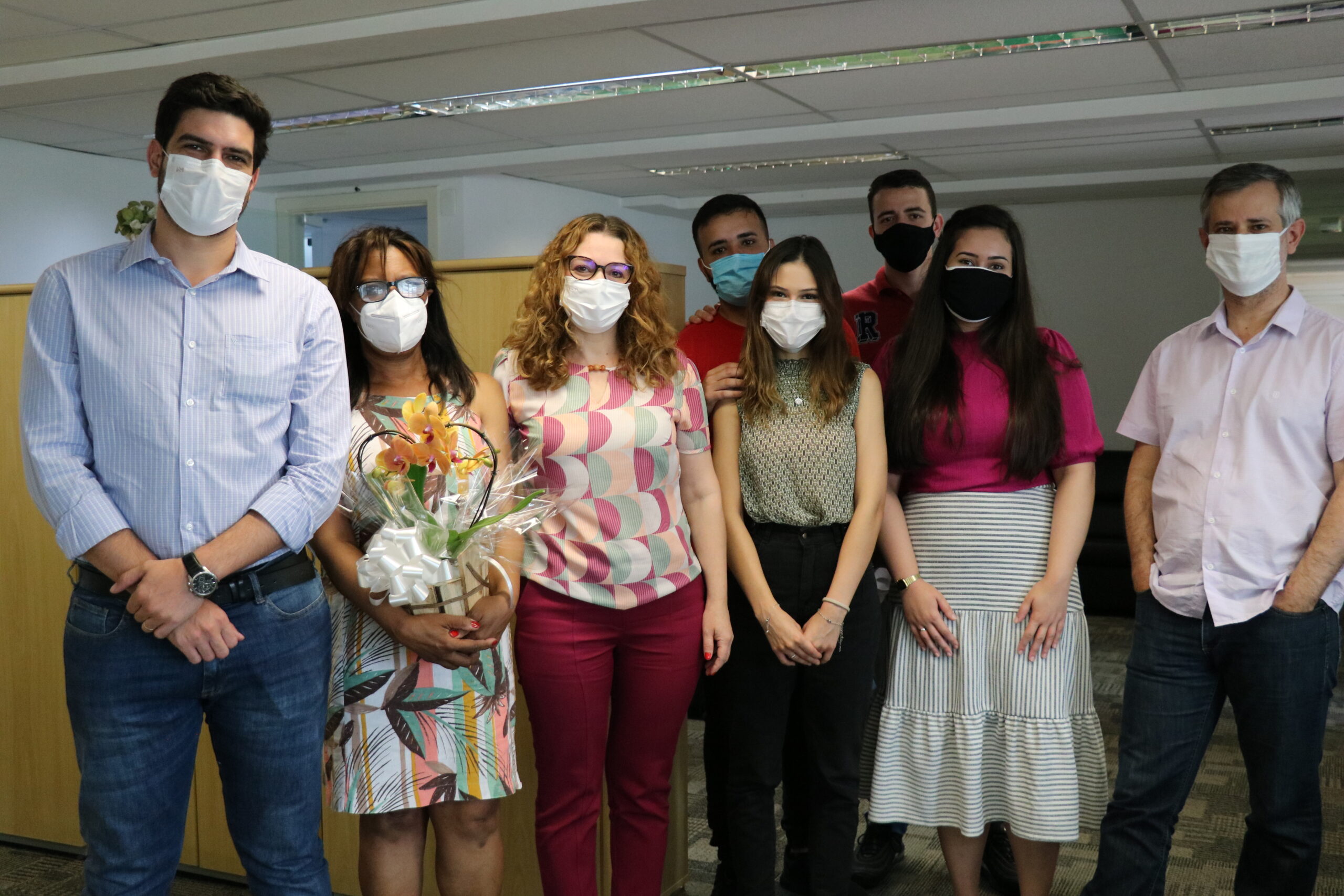 Grupo de oito pessoas em pé usando máscaras, entre eles uma mulher segura arranjo de flores.