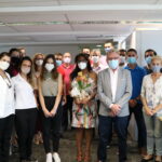 Dezoito pessoass em pé e com máscaras , Mulher no centro da imagem segura um arrajno de flores .