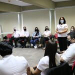 Funcionários das Unidades Regionais sentados de máscara sendo orientados por uma colaboradora do Conselho que está em pé.