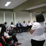 Colaboradora do Conselho está em pé, de costas para a câmera e de frente para os funcionários das Unidades Regionais do CRMV-SP sentados formando meia-lua e de máscaras. Entre eles está o presidnete do Conselho Odemilson Donizete Mossero.