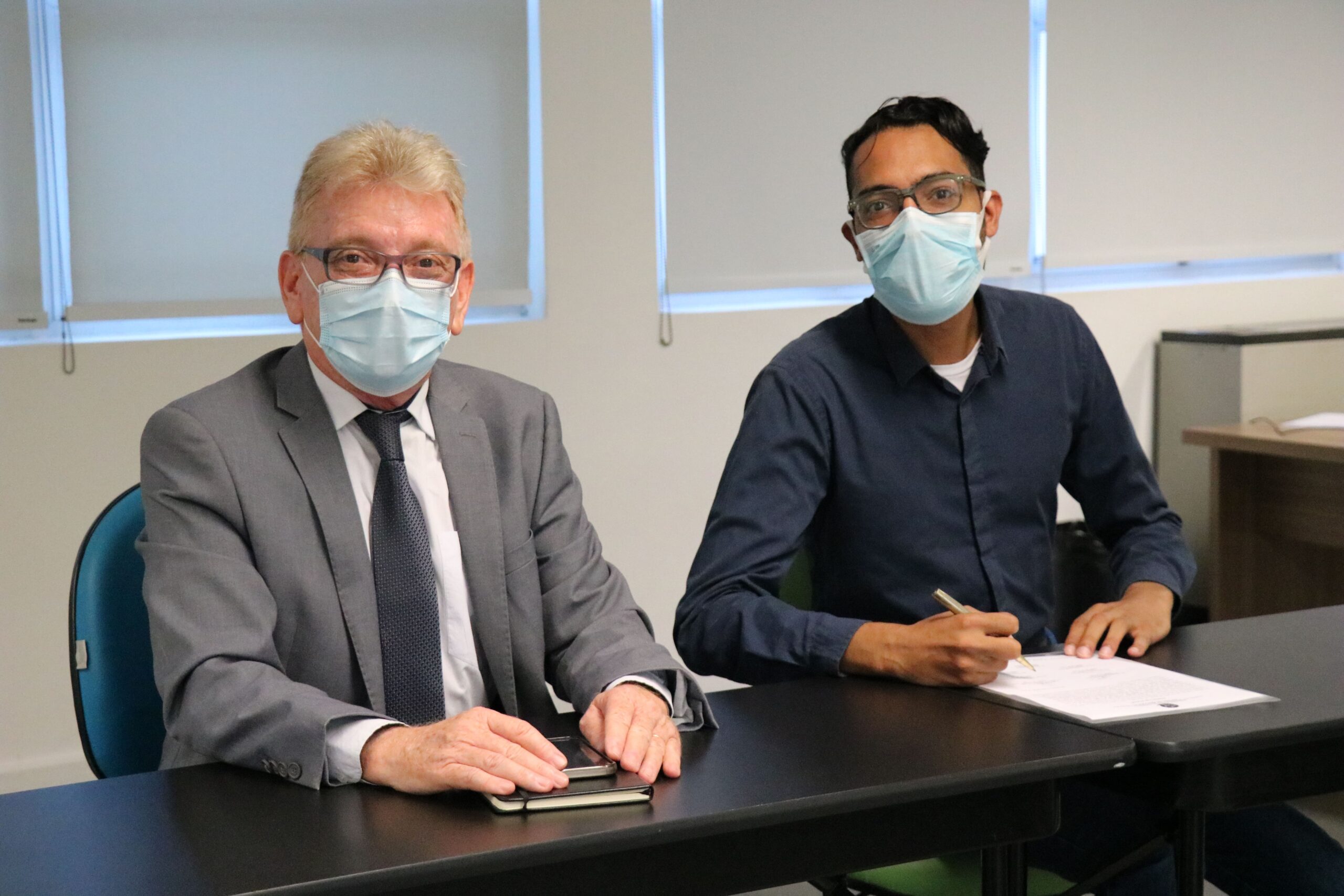 Na foto estão sentados lado a lado e de máscara, posando para a câmera, o presidente do CRMV-SP e o o médico-veterinário e zootecnista João Paulo Fernandes Santos, que faz a menção de assinar o termo de posse como integrante da Comissão de Nutrição Animal.