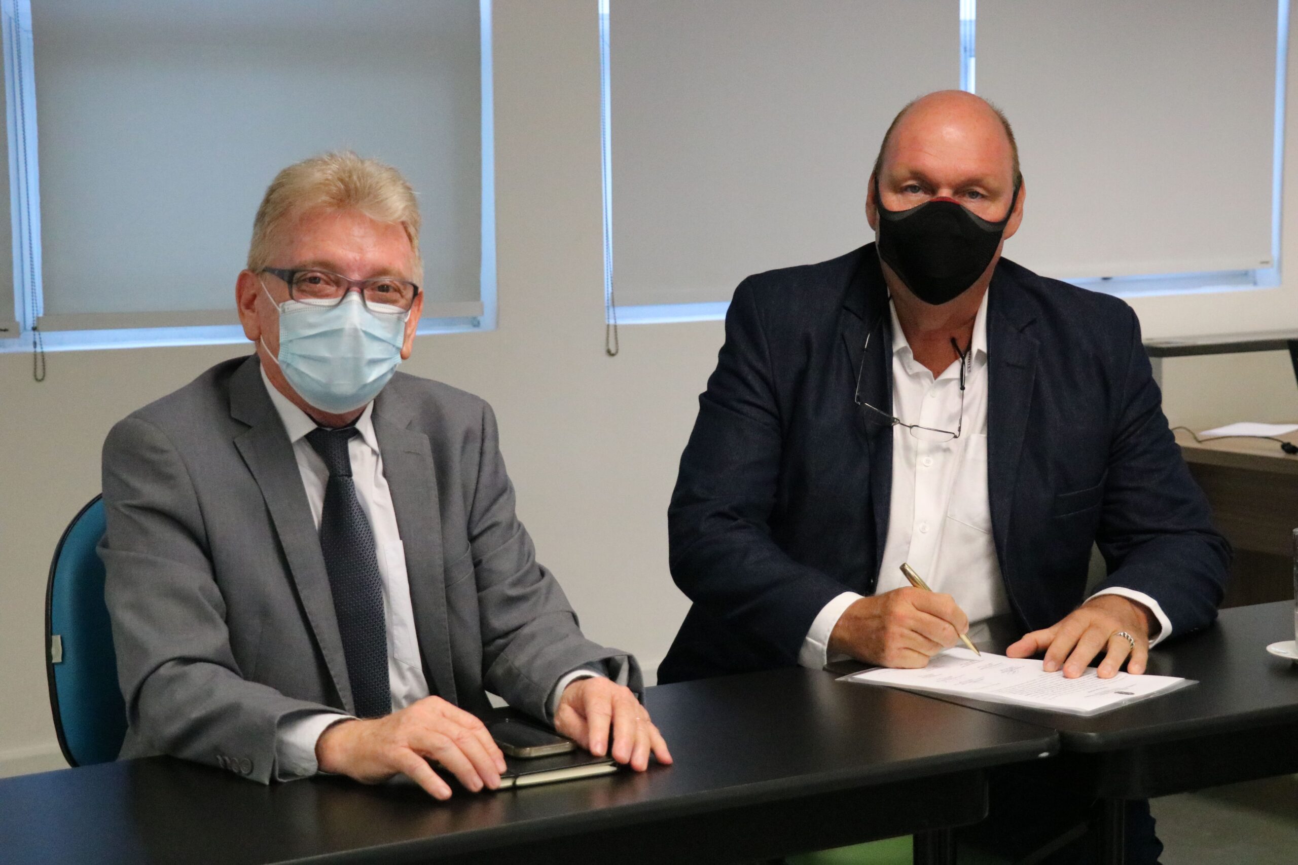 Na foto estão sentados lado a lado e de máscara, posando para a câmera, o presidente do CRMV-SP e o o médico-veterinário Rodolfo Claudio Spers, que faz a menção de assinar o termo de posse como integrante da Comissão de Nutrição Animal.