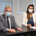 Na foto estão sentados lado a lado e de máscara, posando para a câmera, o presidente do CRMV-SP e a zootecnista Thalita Oliveira Cucki, que faz a menção de assinar o termo de posse como integrante da Comissão de Nutrição Animal.