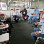 Integrantes da Comissão de Aquicultura estão sentados em carteiras universitárias dispostas em forma de U. Em destaque está o vice-presidente do Conselho, Fernando Gomes Buchala falando e gesticulando.