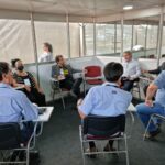 Integrantes da Comissão de Aquicultura, vice-presidente do CRMV-SP e presidente da Peixes Br estão sentados em carteiras universitárias dialogando. Alguns integrantes estão de costas para a câmera.
