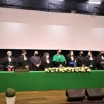 Na foto aparece a mesa de honra composta da solenidade de colação de grau, da qual o vice-presidente do CRMV-SP faz parte, ao lado do diretor, da vice-diretora e de docentes da FMVZ-USP. A mesa está decorada com uma toalha verde, flores brancas e os canudos dos diplomas que serão entregues.