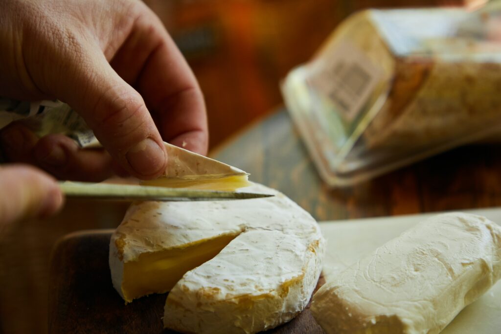 Mão masculina utiliza uma faca para cortar uma fatia de um queijo amarelado curado