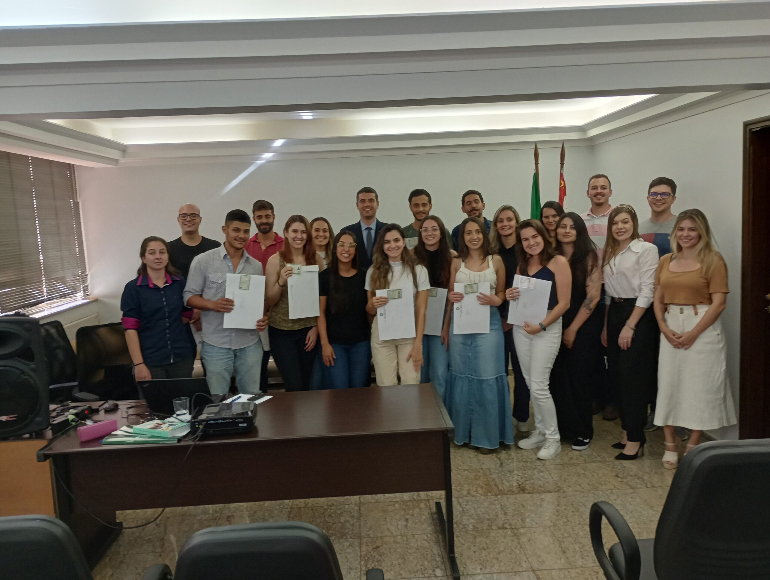 Novos profissionais que receberam a cédula de identidade posam juntos em pé mostrando os novos documentos.