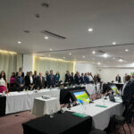 Imagem mostra pessoas dispostas em formato quadrado, com mesas na frente de cada um delas.