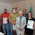 Novos profissionais que receberam a cédula de identidade posam juntos em pé mostrando os novos documentos, juntamente com o Presidente do CRMV-SP, Odemilson Mossero e com o Secretário-geral, Fernando Buchala.