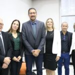 Na foto estão três homens e três mulheres. Eles estão posicionados lado a lado e sorriem para a foto.