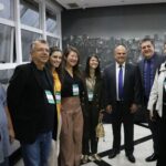 Na foto há quatro homens e quatro mulheres, coordenadores de instituições de ensino superior, representantes da ABHV e do CRMV-SP. Todos estão de pé, sorriem para a câmera e estão posicionados lado a lado a frente de um painel em preto e branco da cidade de São Paulo.