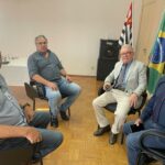 Na imagem estão quadro homens sentados. Eles estão olhando e sorrindo para a câmera. São o diretor regional da CDA, o representante regional, o presidente e o secretário-geral do CRMV-SP. Ao fundo as bandeiras de São Paulo e do Brasil.