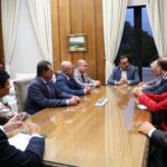 Na imagem estão nove representantes do CRMV-SP, sendo duas mulher e sete homens, sentados entorno de uma mesa de madeira. Na cabeceira, o vice-governador. Ao fundo uma janela com cortinas beges e as bandeiras do estado de São Paulo e do Brasil.