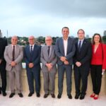 Na imagem estão nove representantes do CRMV-SP, sendo duas mulheres e sete homens, e o vice-governador de São Paulo. Estão todos de pé, lado a lado, e sorriem para a câmera. Ao fundo o céu nublado e a cidade de São Paulo. Eles estão na varanda do Gabinete do vice-governador.