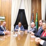 Na imagem estão sete representantes do CRMV-SP, sendo uma mulher e seis homens, sentados entorno de uma mesa de madeira. Na cabeceira, o vice-governador. Ao fundo uma janela com cortinas beges e as bandeiras do estado de São Paulo e do Brasil.