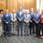 Na imagem estão nove representantes do CRMV-SP, sendo duas mulheres e sete homens, e o vice-governador de São Paulo. Estão todos de pé, lado a lado, e sorriem para a câmera. Ao fundo uma parede de madeira. Eles estão na sala do Gabinete do vice-governador.