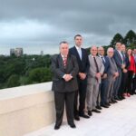 Na imagem estão nove representantes do CRMV-SP, sendo duas mulheres e sete homens, e o vice-governador de São Paulo. Estão todos de pé, lado a lado, e sorriem para a câmera. A foto foi feita de forma lateralizada, por isso, ao lado esquerdo dá para ver o céu nublado e a cidade de São Paulo. Eles estão na varanda da sala do vice-governador.