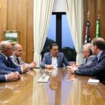 Na imagem estão seis representantes do CRMV-SP, sendo uma mulher e cinco homens, sentados entorno de uma mesa de madeira. Na cabeceira, o vice-governador. Ao fundo uma janela com cortinas beges.