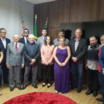 Na foto estão todos os representantes do CRMV-SP e da associação de médicos-veterinários de Piracicaba, o diretor do DBEA, o presidente da Câmara Municipal de Piracicaba e vereadores. Estão todos de pé posando e sorrindo para a câmera. São 11 homens e duas mulheres no total. Na sala há um tapete vermelho redondo a frente deles, e bandeiras do Brasil, do estado de São Paulo e do município atrás deles, assim como uma televisão desligada.