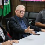 Na imagem aparecem o integrante da Comissão de Saúde Ambiental, a esquerda, o presidente do CRMV-SP, ao centro, e o presidente da Câmara Municipal, a direita. Eles estão sentados ao entorno de uma mesa de cor branca. O presidente do Conselho está com a fala e também gesticula com as mãos. Os demais o observam.