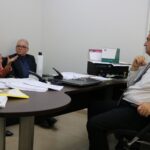 Na foto aparecem a tesoureira e o presidente do CRMV-SP sentados em um sofá, e o delegado da seccional de Piracicaba sentado atrás de uma mesa cheia de papéis. A tesoureira dirige a fala ao delegado e se expressa também gesticulando as mãos.