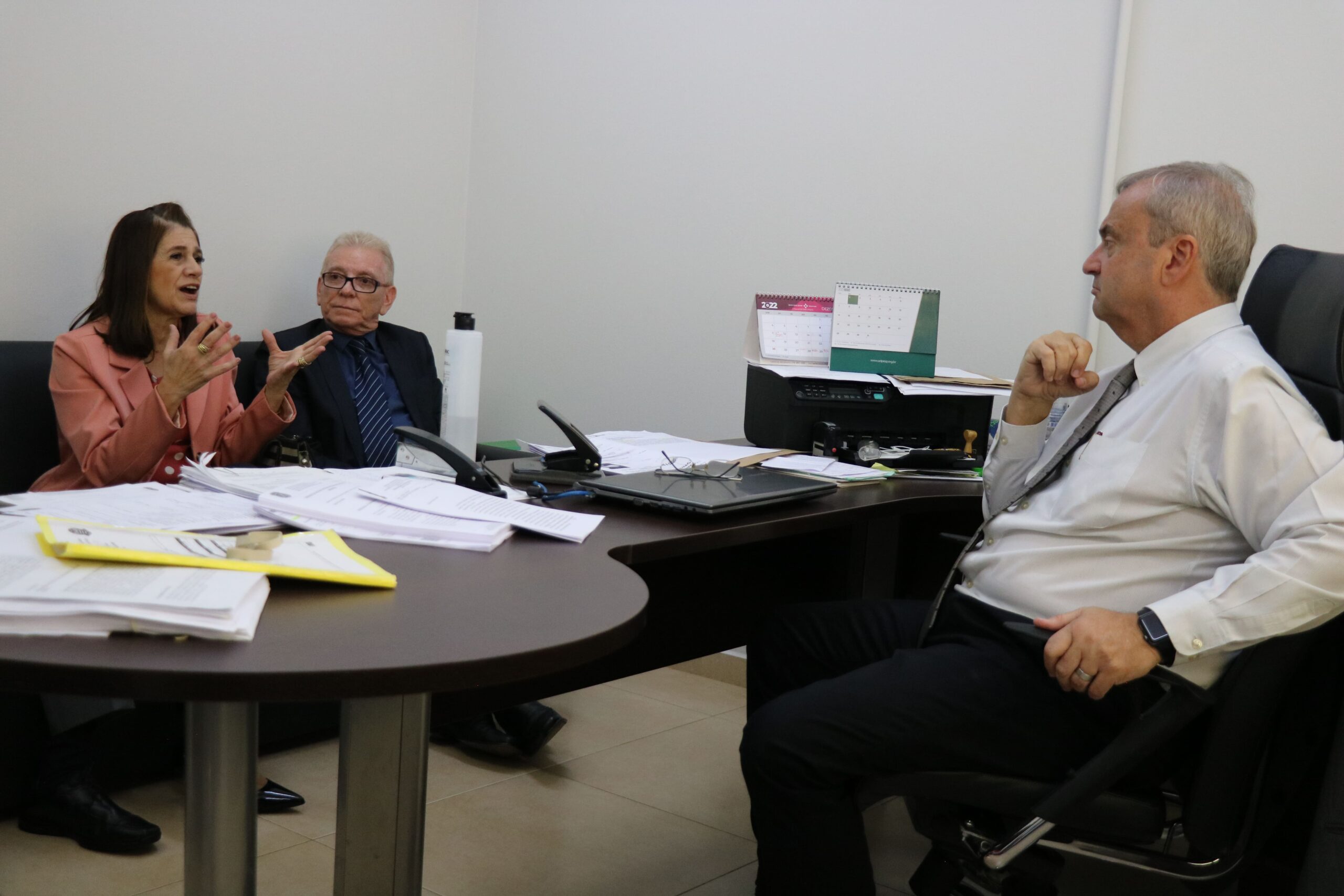 Na foto aparecem a tesoureira e o presidente do CRMV-SP sentados em um sofá, e o delegado da seccional de Piracicaba sentado atrás de uma mesa cheia de papéis. A tesoureira dirige a fala ao delegado e se expressa também gesticulando as mãos.