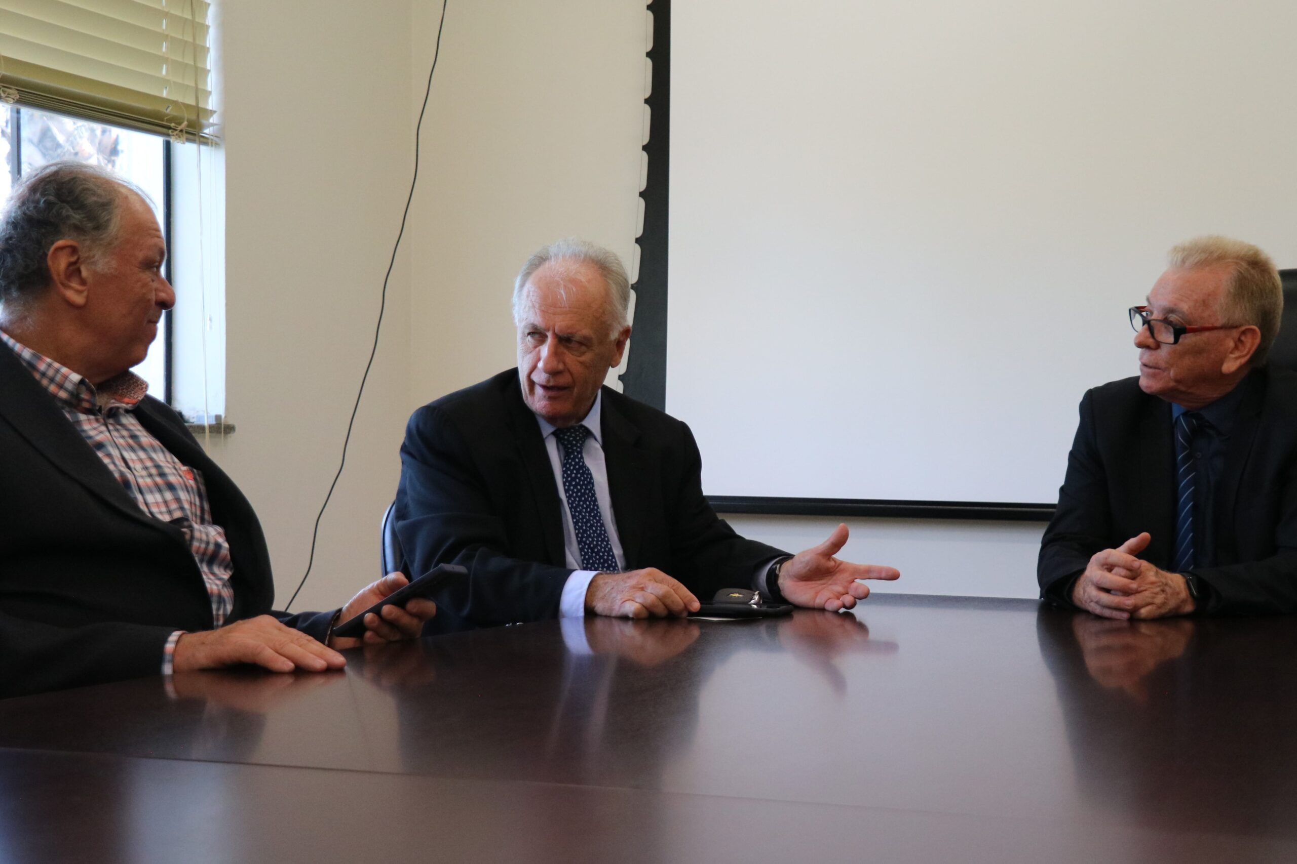 Na foto aparecem o integrante da Comissão de Saúde Ambiental, a esquerda, o delegado de polícia diretor do Deinter 9, ao centro, e o presidente do CRMV-SP, a direita. Eles vestem terno e estão sentados ao entorno de uma mesa de madeira conversando.