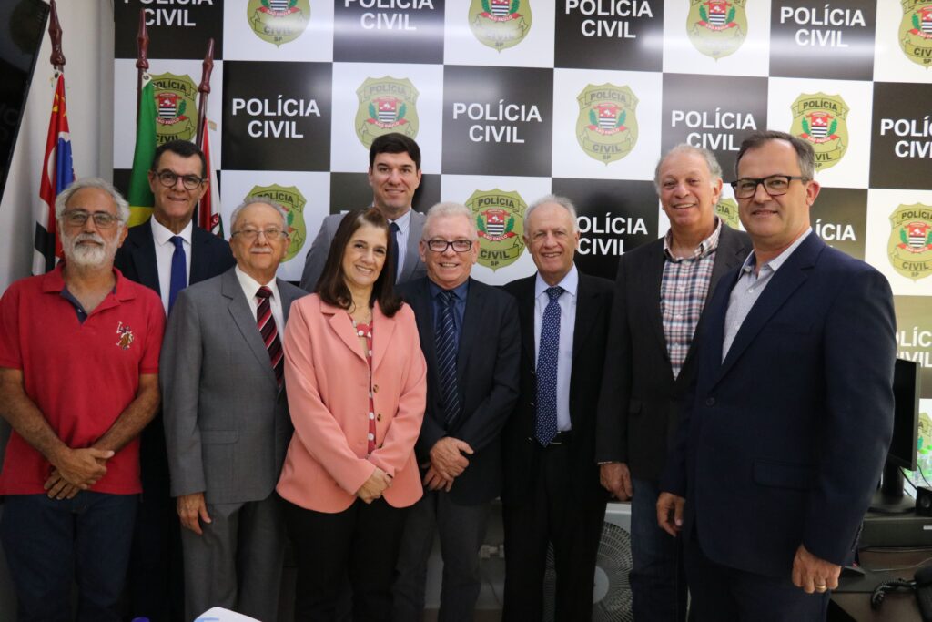 Na foto os representantes do CRMV-SP, da associação de médicos-veterinários de Piracicaba e o delegado de polícia diretor do Deinter 9 estão de pé, posicionados lado a lado e em frente a um painel da polícia civil. Todos sorriem para a câmera.