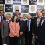 Na foto os representantes do CRMV-SP, da associação de médicos-veterinários de Piracicaba e o delegado de polícia diretor do Deinter 9 estão de pé, posicionados lado a lado e em frente a um painel da polícia civil. Todos sorriem para a câmera.