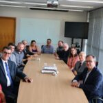 Na foto estão os representantes do CRMV-SP e da associação de médicos-veterinários de Piracicaba com uma vereadora da cidade, o diretor do DBEA, o secretário de Saúde e o prefeito de Piracicaba. Estão todos sentados no entorno de uma mesa retangular de madeira. O prefeito está na cabeceira. Todos estão olhado para a câmera. Há 11 homens e duas mulheres.