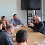 Na foto o destaque é para a fala e gestual do presidente do CRMV-SP, que dirige a fala ao prefeito de Piracicaba. Estão todos sentados ao entorno de uma mesa retangular de madeira. Aparecem ainda mais duas mulheres e cinco homens, os quais participam da reunião.