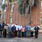 Na foto aparecem os representantes do CRMV-SP e da Unimep. Estão todos de pé, posam e sorriem para a câmera, e estão posicionados em frente a uma construção história com tijolos de barro aparentes cercada por uma jardim com palmeiras. São 10 homens e três mulheres no total.